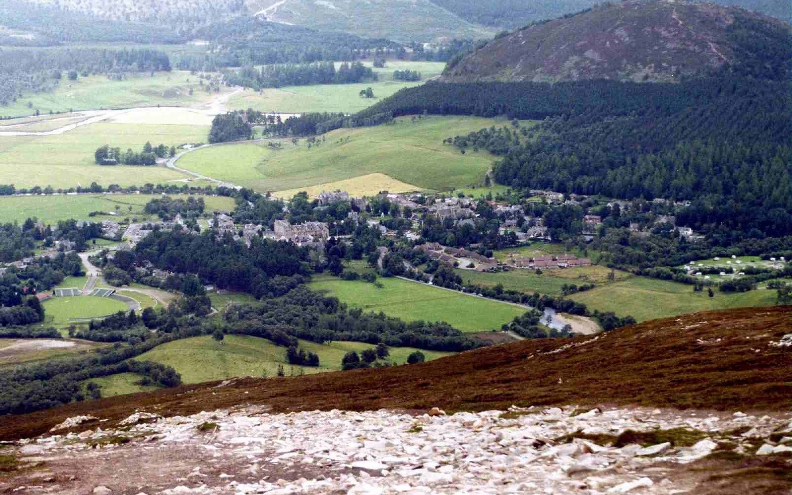 Aerial view of Braemar village nestled in a green valley below forested hills