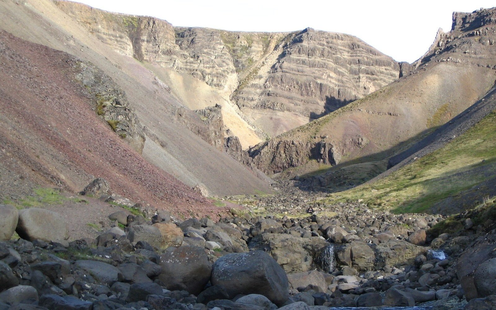 Rocky mountain valley with layered cliffs and a boulder-strewn streambed at Húsafell
