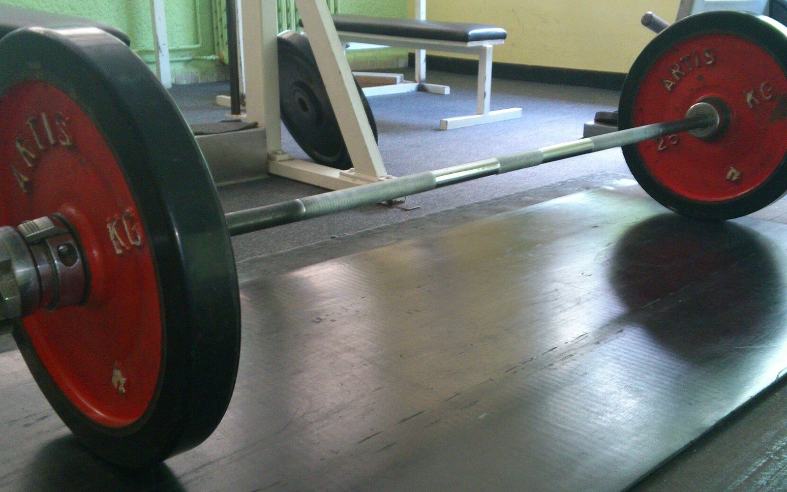 Loaded barbell with red weight plates resting on a gym floor mat