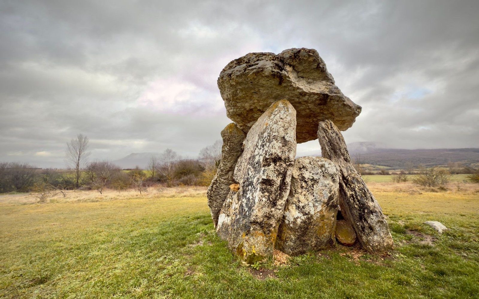 A stone dolmen with a large flat capstone resting on upright rocks in a grassy field