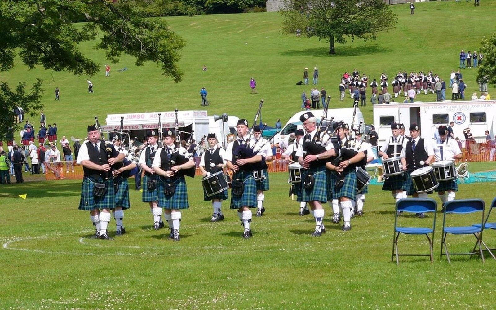 Pipers and drummers in kilts march across a grassy field at a highland games